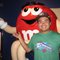 A man standing next to a giant m & m 's character.